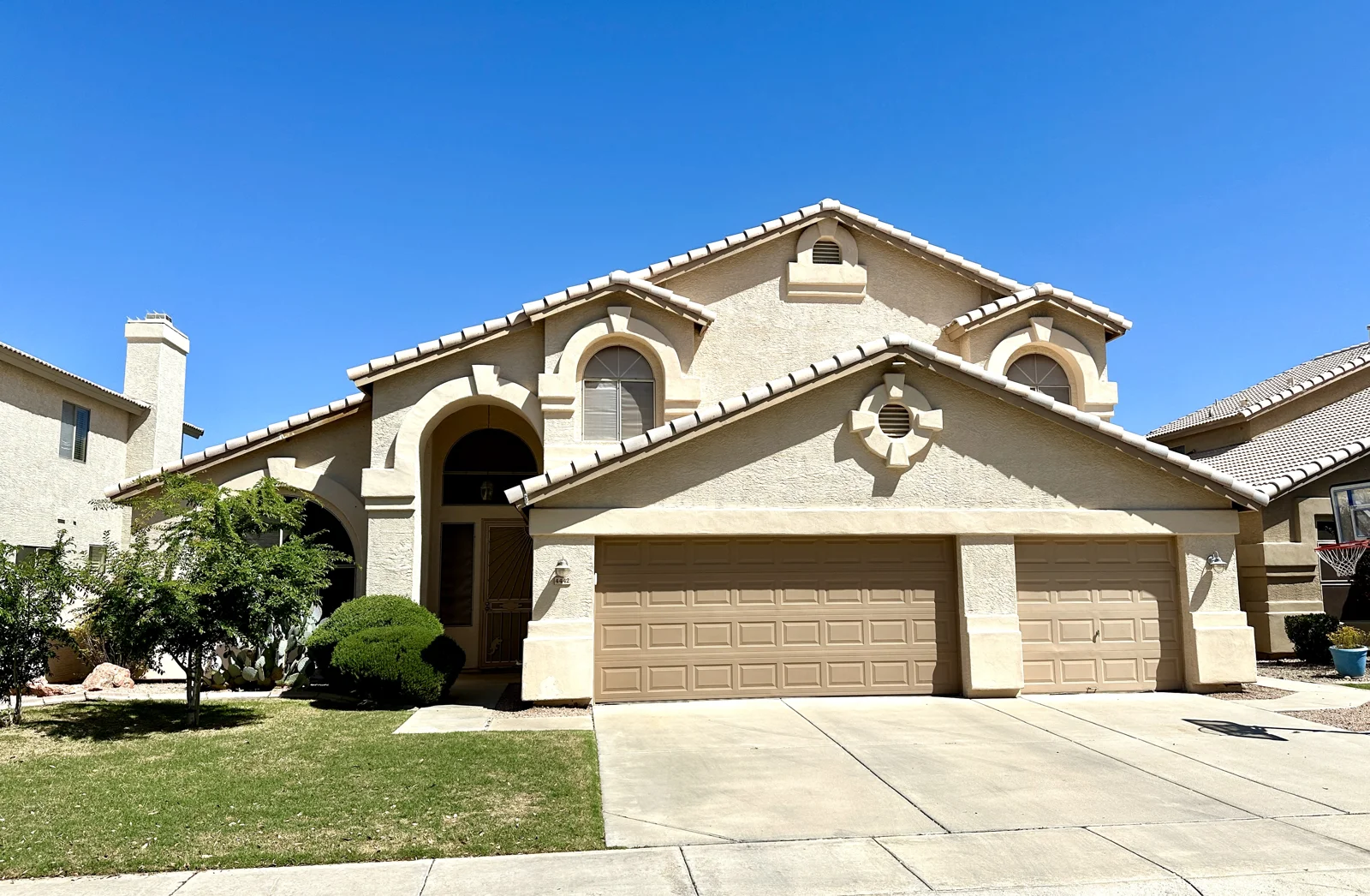 Two-story stucco home with an arched entry and a green front lawn